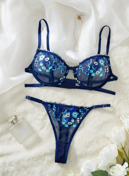 A navy blue sheer mesh lingerie set from The Seventh Muse with blue and white floral embroidery, including a plunge bra with cut-outs and an adjustable thong.
