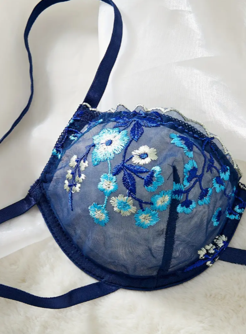 A navy blue sheer mesh lingerie set from The Seventh Muse with blue and white floral embroidery, including a plunge bra with cut-outs and an adjustable thong.