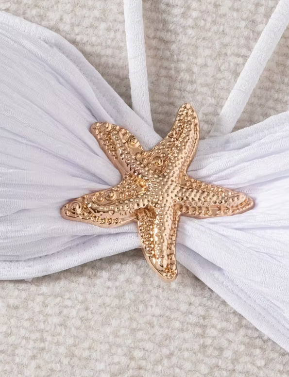 White three-piece bikini set for women featuring a starfish embellishment, halter neck bandeau top, matching bikini bottom, and wrap cover-up skirt – chic beachwear from The Seventh Muse.