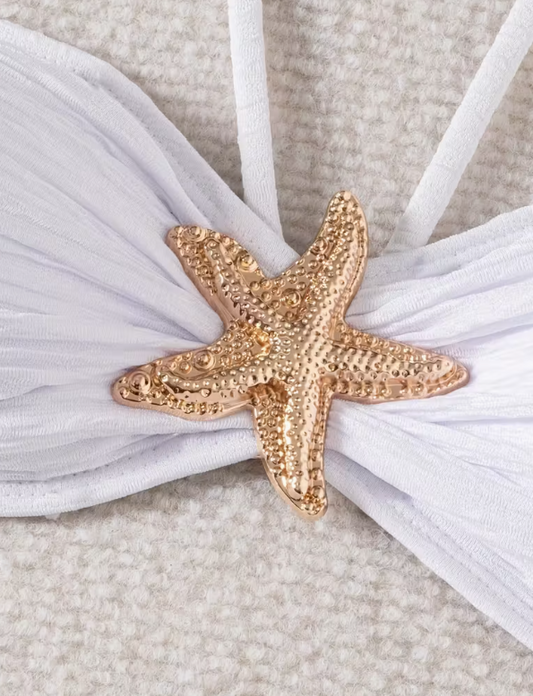 White three-piece bikini set for women featuring a starfish embellishment, halter neck bandeau top, matching bikini bottom, and wrap cover-up skirt – chic beachwear from The Seventh Muse.