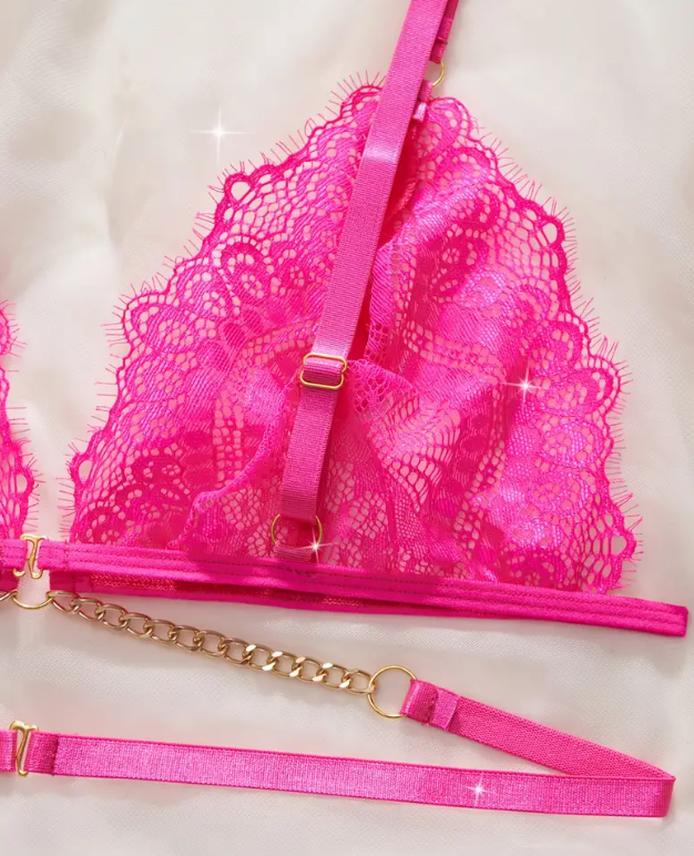 Close-up of a vibrant hot pink sheer lace bralette featuring a deep plunge, thin adjustable straps, and a decorative gold chain below the cups.