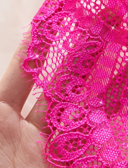 Close-up of a vibrant hot pink sheer lace bralette featuring a deep plunge, thin adjustable straps, and a decorative gold chain below the cups.