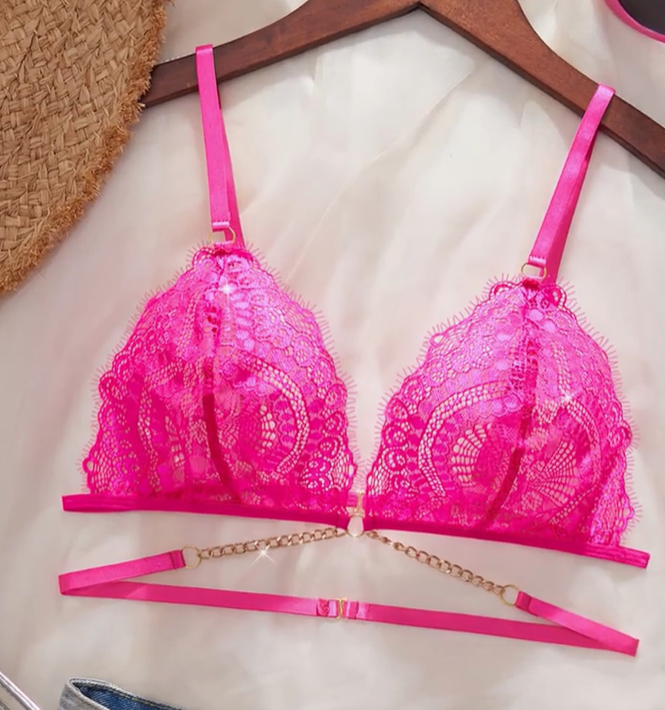 Close-up of a vibrant hot pink sheer lace bralette featuring a deep plunge, thin adjustable straps, and a decorative gold chain below the cups.