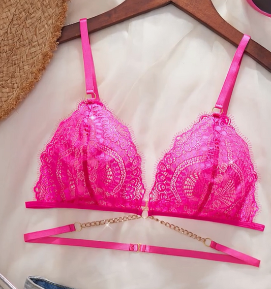 Close-up of a vibrant hot pink sheer lace bralette featuring a deep plunge, thin adjustable straps, and a decorative gold chain below the cups.