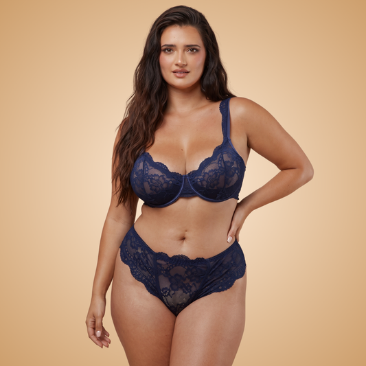 A woman modeling a navy blue lace bra and matching high-waisted panties against a solid beige background.