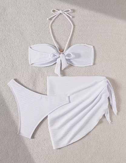 White three-piece bikini set for women featuring a starfish embellishment, halter neck bandeau top, matching bikini bottom, and wrap cover-up skirt – chic beachwear from The Seventh Muse.