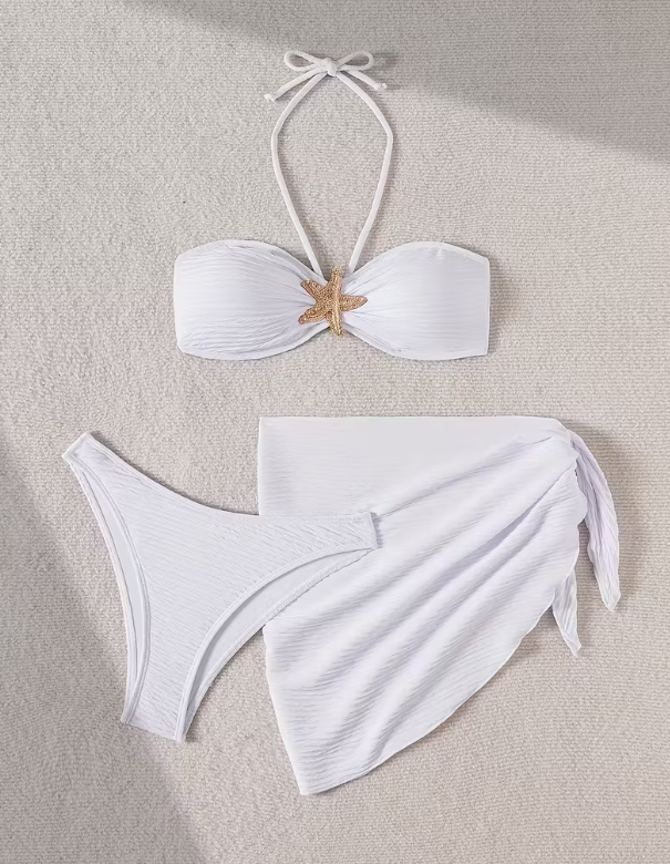 White three-piece bikini set for women featuring a starfish embellishment, halter neck bandeau top, matching bikini bottom, and wrap cover-up skirt – chic beachwear from The Seventh Muse.