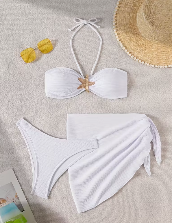 White three-piece bikini set for women featuring a starfish embellishment, halter neck bandeau top, matching bikini bottom, and wrap cover-up skirt – chic beachwear from The Seventh Muse.