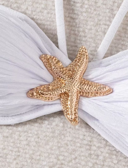 White three-piece bikini set for women featuring a starfish embellishment, halter neck bandeau top, matching bikini bottom, and wrap cover-up skirt – chic beachwear from The Seventh Muse.