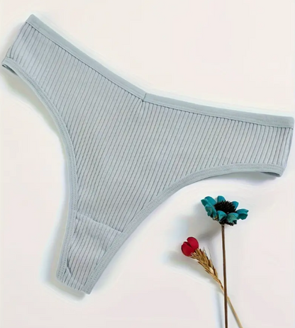 A set of four cotton panties in black, white, beige, and blue colors, displayed on a soft, textured surface.