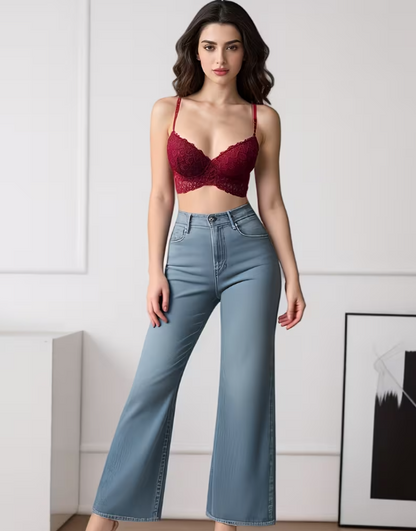 Woman wearing a red bralette and blue jeans against a white wall.