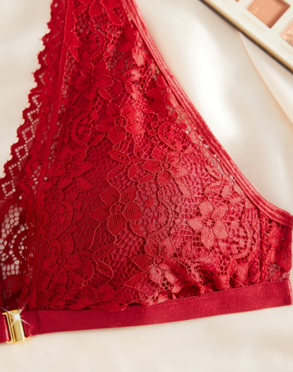 Romantic red lace lingerie set from The Seventh Muse featuring a deep V-neck scalloped lace bralette with a delicate gold front clasp and matching lace bikini briefs with a soft red bow detail. Styled on elegant ivory satin with red florals and subtle gold accents, creating a luxurious Valentine-inspired aesthetic that reflects confidence, femininity, and intimate elegance.