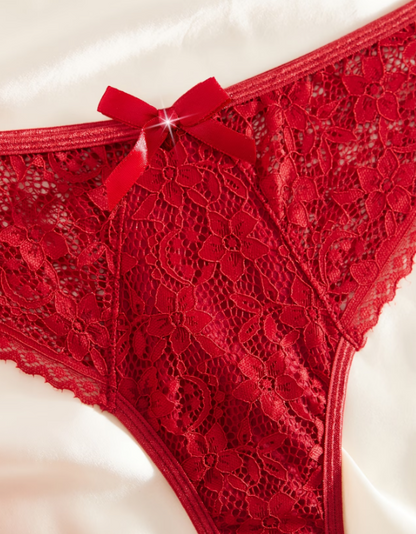 Romantic red lace lingerie set from The Seventh Muse featuring a deep V-neck scalloped lace bralette with a delicate gold front clasp and matching lace bikini briefs with a soft red bow detail. Styled on elegant ivory satin with red florals and subtle gold accents, creating a luxurious Valentine-inspired aesthetic that reflects confidence, femininity, and intimate elegance.