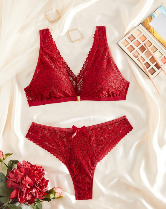 Red lace bra and panties set on a white fabric background with flowers and makeup palette.