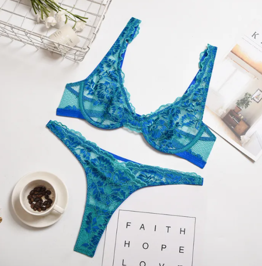 Blue lace lingerie set on a white surface with a cup of coffee and flowers.